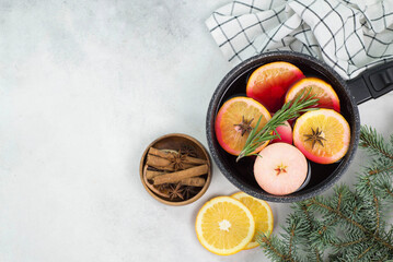 Mulled wine with pieces of orange and apples in a black ladle on a grey background.