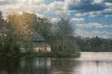 Scenic view of peaceful landscape with house at a lake and leafless trees under cloudy blue sky,...