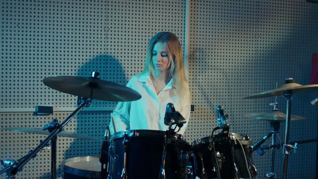 Blonde girl is learning to play drums, cymbals. Female drummer is rehearsing before concert. Young woman tympanist performs musical composition on percussion instruments in recording studio