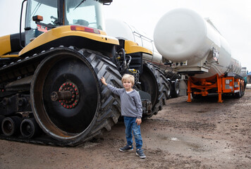 portrait of a little boy standing near the huge caterpillar wheels of a bulldozer. the boy's...