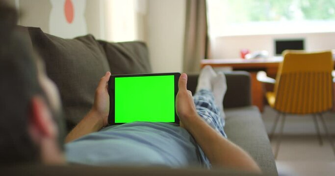 Man, green screen and tablet for communication, branding and logo design mockup while on sofa in living room at house. Male with technology for website, space and mobile app with home wifi connection