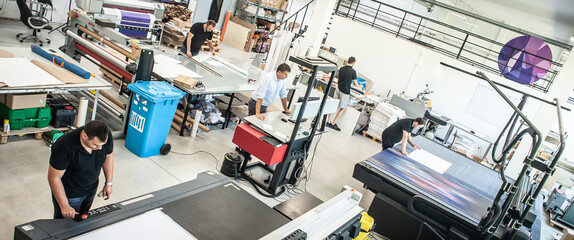 In a large modern printing plant, operators work on various types of machines for printed material
