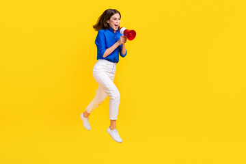 Fototapeta na wymiar Full length photo of charming excited girl dressed blue shirt jumping high shouting toa empty space isolated yellow color background