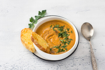 Vegan cream soup of red lentils and vegetables with coconut milk  sprinkled with chopped parsley in a white bowl and cheese croutons on a light gray background