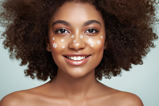 Beauty portrait of African girl with snowflakes her face. Beautiful black woman. Cosmetics, makeup and fashion. Beauty model with curly afro hair. Christmas or New Year festivities makeup