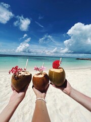 Tropical coconut cocktails in the hands of three people on the beach of the Maldives. Three coconut drinks at a luxury tropical resort.