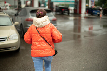 Girl goes to gas station with gasoline. Woman in parking lot. Man on street. Petrol station in city.