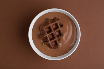 Waffles with chocolate topping in chocolatte pudding on brown background.