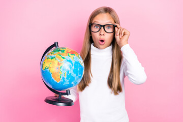 Fototapeta premium Portrait of impressed smart girl hold globe arm touch eyeglasses open mouth isolated on pink color background