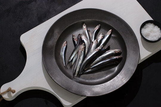 Raw small fishes in plate on dark background