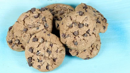 Poster Closeup of round American cookies with chocolate chips on a light blue bowl and white background © Giuseppe Silvestri/Wirestock Creators