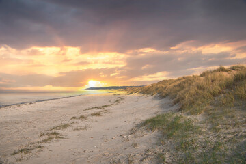 Beach crossing in Denmark by the sea. Dunes, sand water and clouds on the coast.