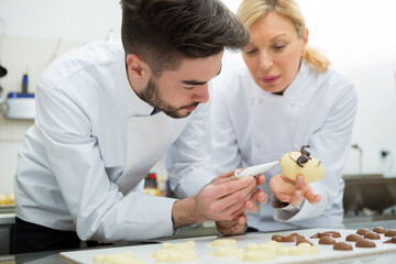 mature female making chocolate eggs with apprentice