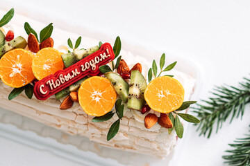 Festive meringue roll with an inscription and decorated with fruits and nuts.