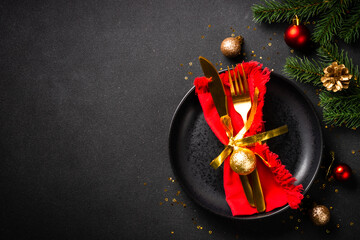 Christmas table with black plate, golden cutlery and holiday decorations. Top view on black.