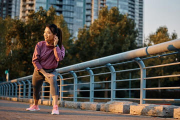 Happy Asian athletic woman warming up on bridge.