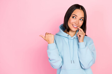Photo of adorable tricky lady wear blue hoodie finger lips pointing thumb empty space isolated pink color background