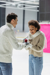 Obraz premium Young man holding proposal ring during date with african american girlfriend on ice rink