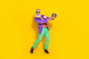 Fototapeta na wymiar Full length photo of positive good mood guy dressed violet velvet jacket holding disco ball dancing isolated yellow color background
