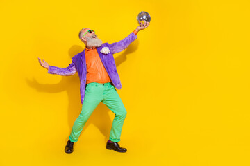 Full length photo of good mood cool guy dressed violet velvet jacket having fun rising disco ball empty space isolated yellow color background