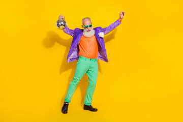 Fototapeta na wymiar Full length photo of cool pretty man wear purple velvet jacket having fun rising discotheque ball isolated yellow color background