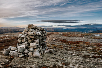 dark moody northern landscape, cairn stack of stones on a top of mountain Rogne in Norway