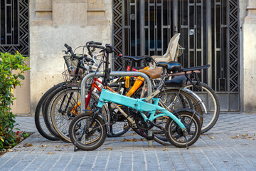 Fototapeta na wymiar Set of different bicycles parked with chains and padlocks on the sidewalk in a street in Barcelona. A bicycle is blue and foldable.