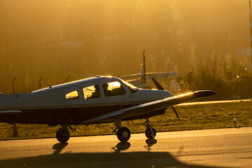 A small propeller plane rolling down the runway in backlight under a yellow sunset sun in sabadell...