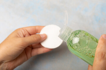 A bottle with micellar water and a cotton pad in female hands. Makeup remover. Facial skin cleansing. Beauty concept. Skin care. Place for text.