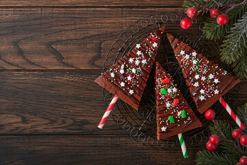 Chocolate brownies Christmas tree with chocolate icing and festive sprinkles on wooden table. Christmas food ideas sweet homemade Christmas holidays pastry concept. Holiday cooking concept. Top view.