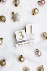 Happy New Year holiday background, calendar with date 31 december and christmas shiny balls on white fake fur. Golden, pale pink color metallic balls, Trend minimal aesthetic pattern, flat lay