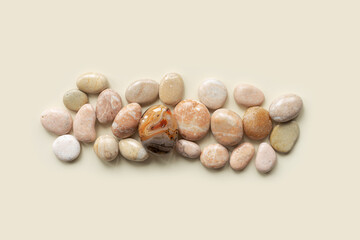 Aesthetic minimal flat lay with sea pebble stones on beige background with copy space. Row from natural smooth stone pastel color and sardonyx gemstone. Summer concept, top view