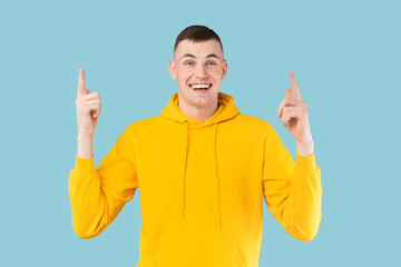 Naklejka premium Look up. Happy caucasian guy pointing fingers upward, showing something over blue background, studio shot