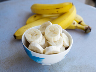 Sliced bananas in a bowl to prepare a fruit salad with whole bananas on the side. Concept of fruits and health.