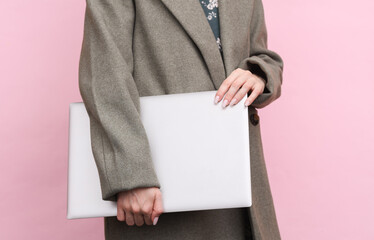 Woman in wool coat holding closed laptop on pink background
