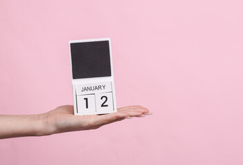 Female hand holding wooden calendar with date January 12 on pink background