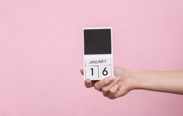 Female hand holding wooden calendar with date January 16 on pink background