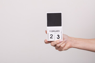 Female hand holding wooden calendar with date February 23 on gray background