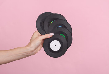 Woman's hand holds a miniature vinyl records on pink background. Music concept