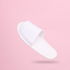 White hotel slippers levitating on a pink background with a shadow