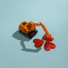 Toy excavator model with hearts on blue background. Love concept, valentine's day, february 14th celebration, creative layout