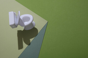 Plastic miniature toilet on a paper cube. Optical illusion. Geometric composition. Minimalistic creative layout