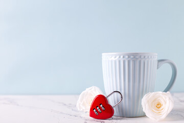St. Valentine day romantic  background. Blue cup with hot drink, white tender roses flowers and red lock in form of heart on white marble background against blue wall. Selective focus. Place for text. - 550666744