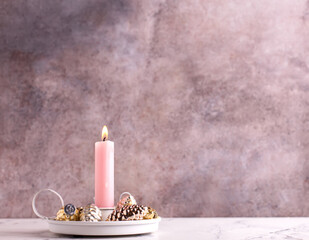 Pink burning candle and golden  and golden and silver decorative cones against pink textured wall. Selective focus is on candle. Place for text. Pink Christmas postcard. - 550666768