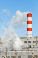 Obraz premium Pollution of the environment, ecology and air. Withdrawal of combustion products of soot, smoke and gases from the pipe of an industrial plant into the atmosphere against the background of a blue sky