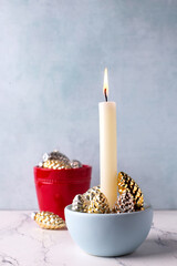 Golden and silver decorative cones and white burning candle against blue  textured wall. Selective focus is on candle. Place for text. - 550666779