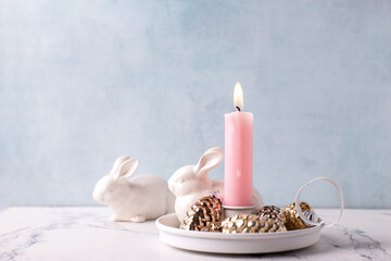 White bunnies and burning pink  candle on white marble background against blue  textured wall. Rabbit is symbol of 2023.. Selective focus is bunny. Place for text. - 550666788