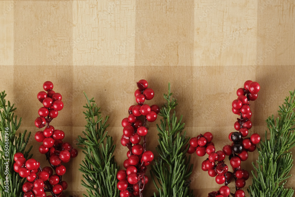 Wall mural Red berries and Christmas greenery on rustic tan plaid background for holiday banner with copy space. - Wall murals