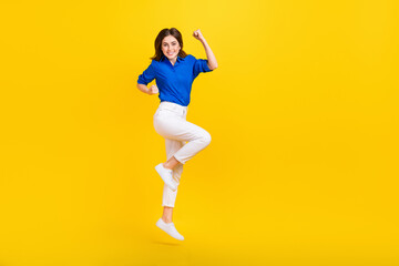 Fototapeta na wymiar Full length photo of impressed lucky girl dressed blue shirt jumping high rising fists empty space isolated yellow color background