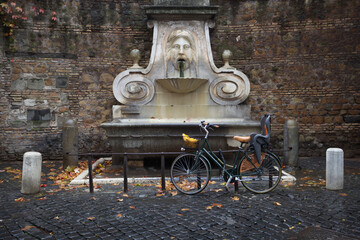 Plakat Parked bicycle with child seat next to an ornamental fountain in Roma. Sustainable urban transport.